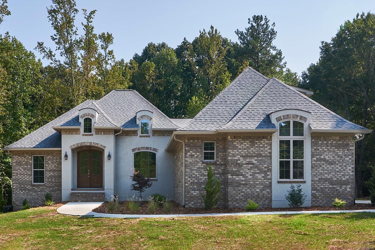 House plan exterior with brick and stucco facade, arched windows, and multiple gabled rooflines.