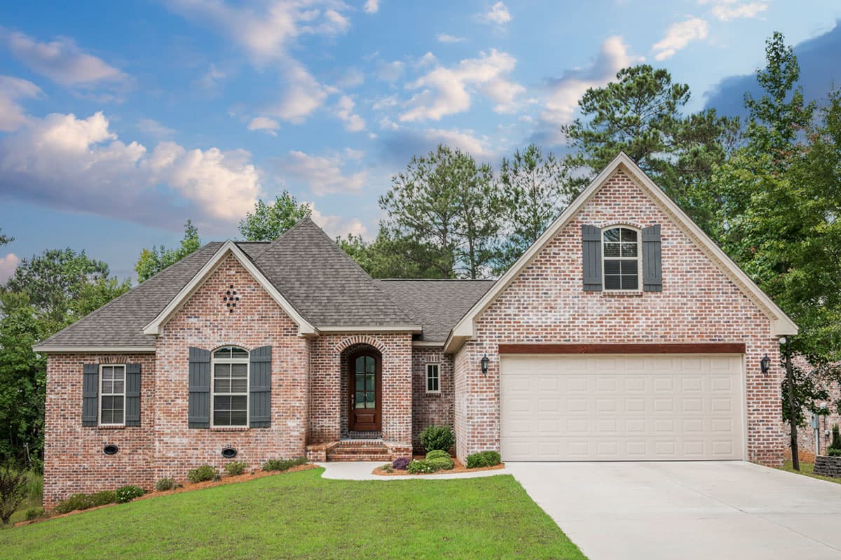 House plan exterior: Traditional brick home with a prominent gable, arched entryway, and attached two-car garage.