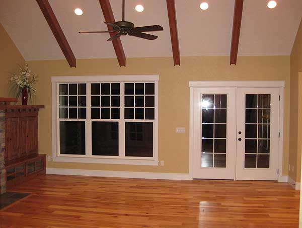 Interior view of a living room with vaulted ceiling, exposed beams, large grid-pane windows, and French doors.