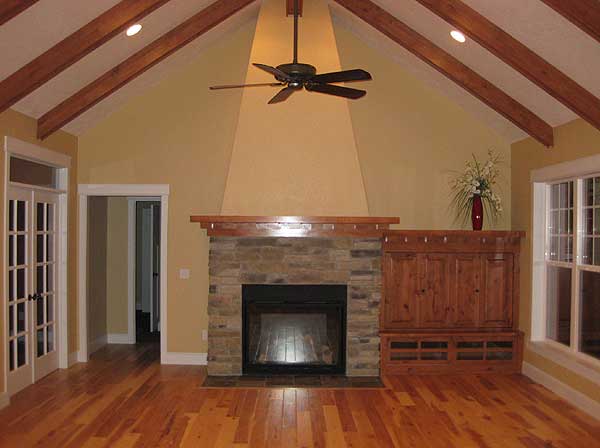 Great room with vaulted beamed ceiling, stone fireplace, built-in media cabinet, and hardwood floors.