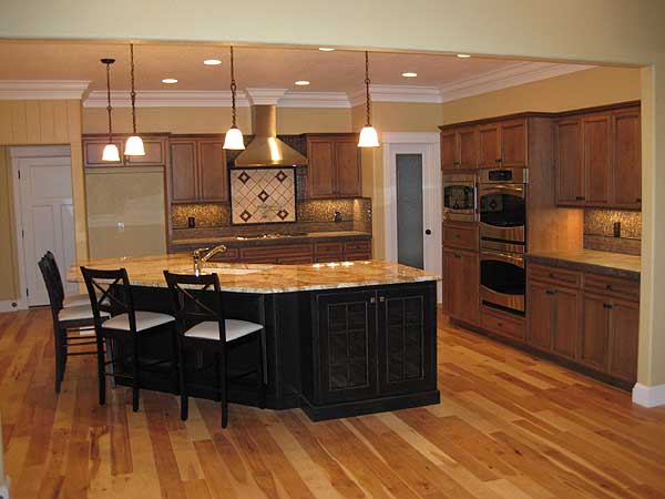 Kitchen interior with large island, granite countertops, wood cabinets, double ovens, and pendant lighting.