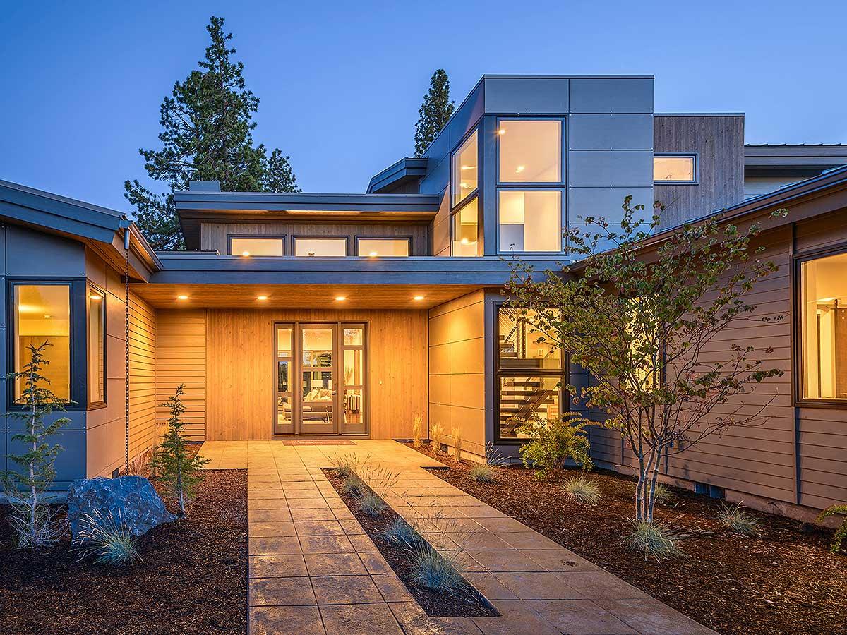 Modern house exterior with wood siding, metal panels, expansive windows, and a covered entryway.