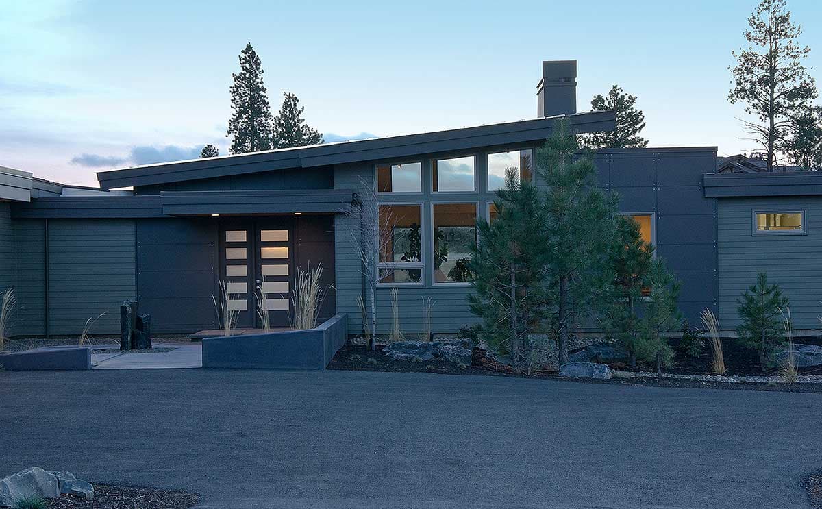 Modern house plan exterior with a low-pitched roof, prominent chimney, large multi-pane window, and double-door entry.