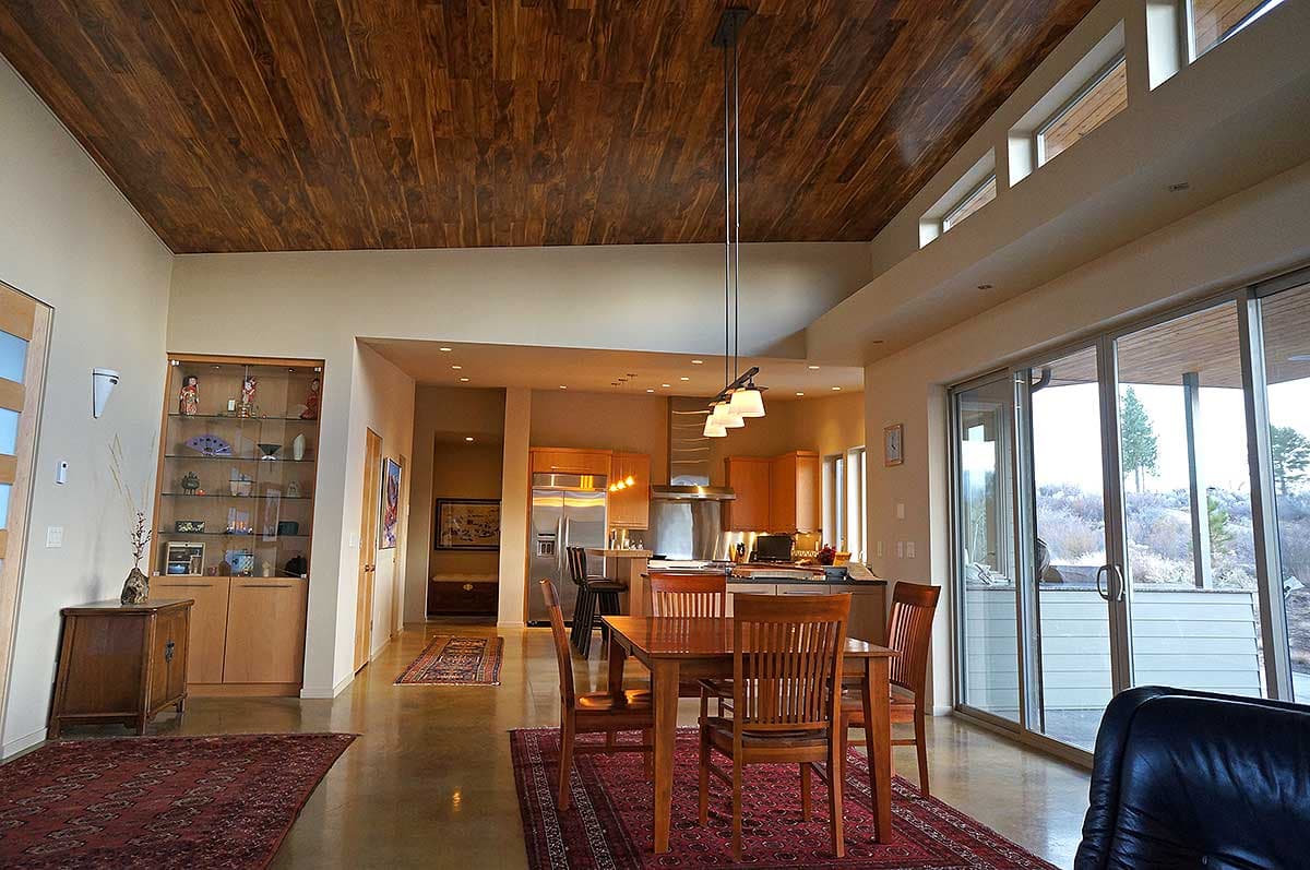 Open concept living area with dining room, kitchen, and large sliding glass doors. Features sloped wood ceiling.