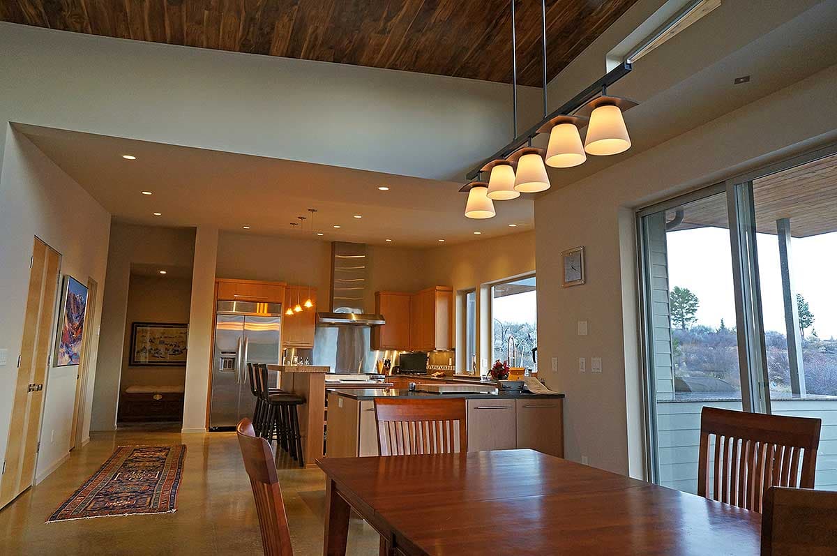 Interior view of a kitchen and dining area with vaulted wood ceiling, island, and large windows.