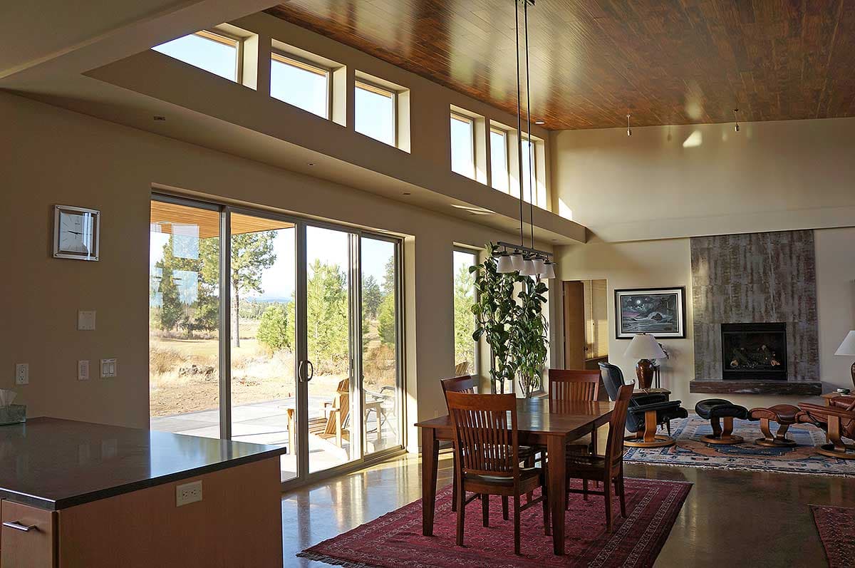 Open concept dining and living area with vaulted wood ceiling, clerestory windows, fireplace, and large sliding glass doors to patio.