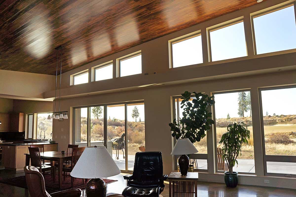 Open-concept living area with wood-paneled vaulted ceiling, large windows, and dining area adjacent to kitchen.