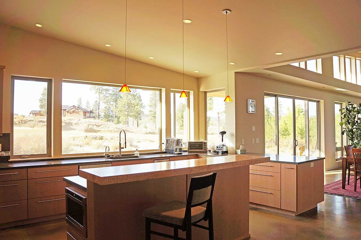 Modern kitchen interior with large windows, island, and vaulted ceiling. Floor-to-ceiling sliding glass doors to the exterior.