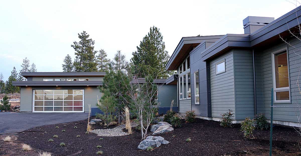 Modern house exterior with a glass garage door, low-pitched rooflines, and horizontal siding.