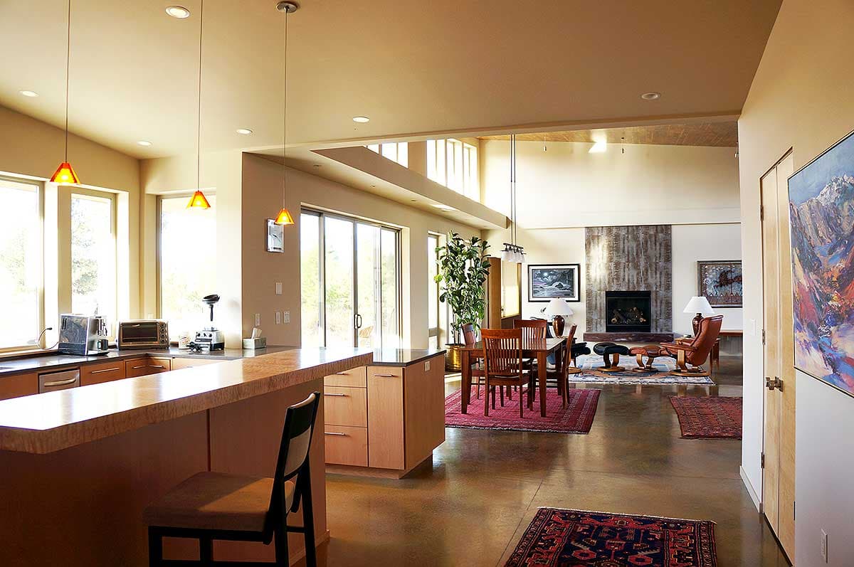 Open-concept interior with kitchen island, dining area, and living room featuring a stone fireplace and vaulted ceiling.