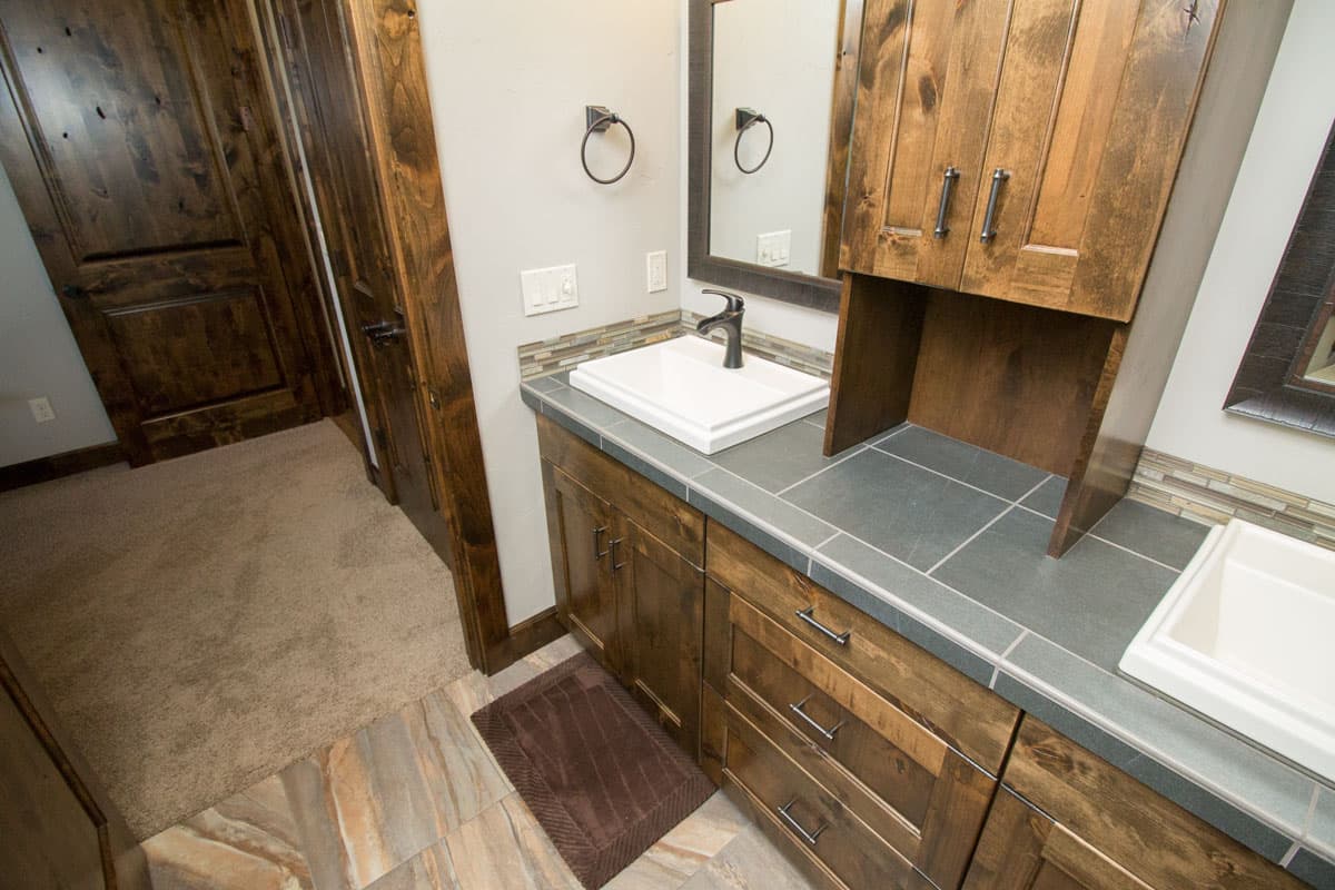 Bathroom vanity with wood cabinetry, dark tile countertop, vessel sink, and tile backsplash.