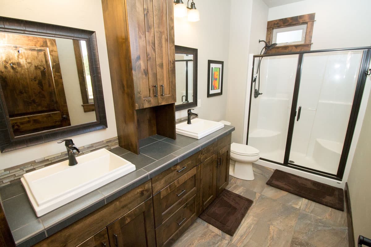Bathroom with double vanity, wood cabinets, walk-in shower with glass doors, and tile flooring.