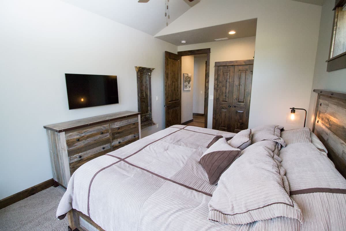 Bedroom with vaulted ceiling, mounted TV, rustic dresser, and double wood doors leading to hallway.