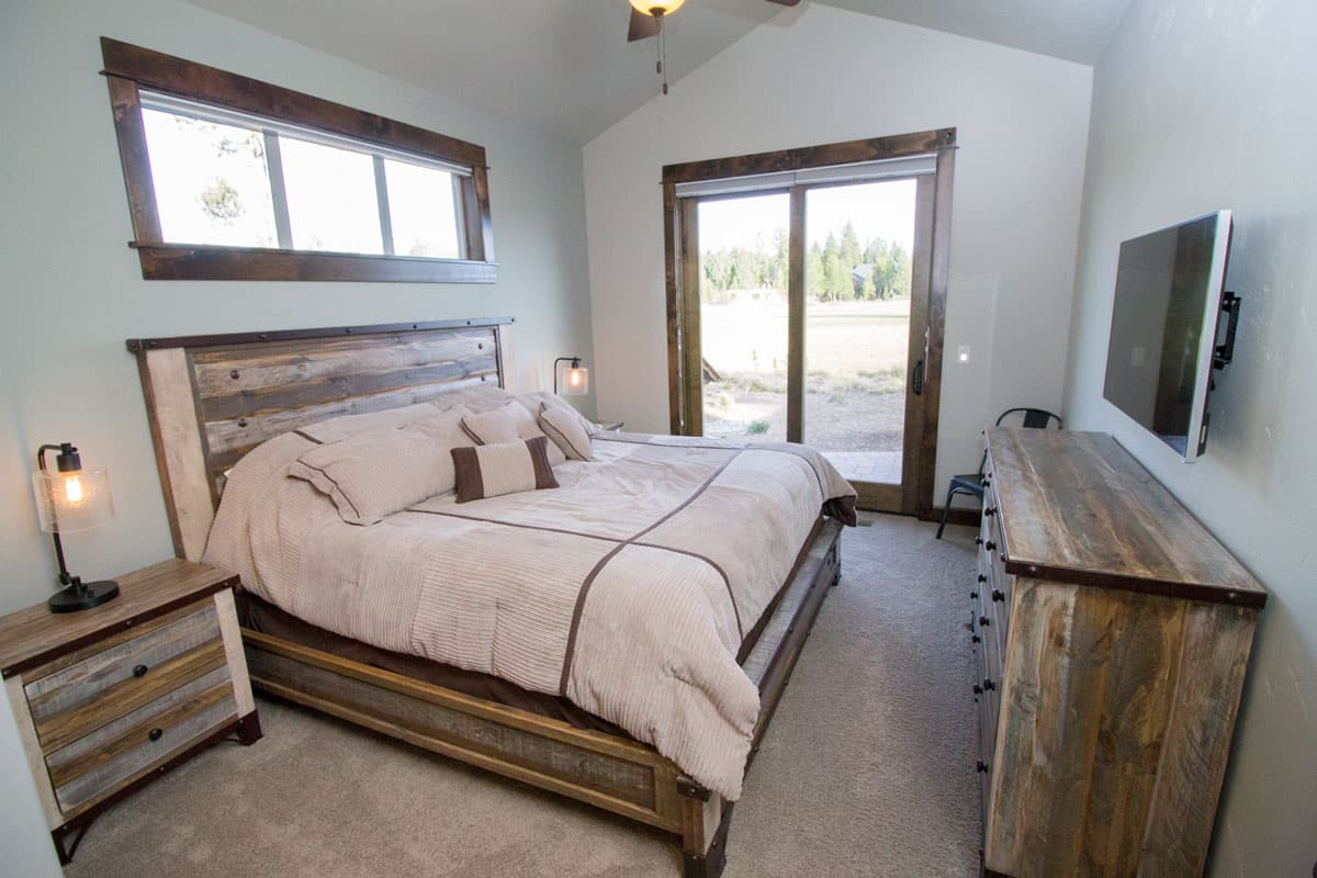 Primary bedroom with vaulted ceiling, king bed, sliding glass door, and mounted TV.