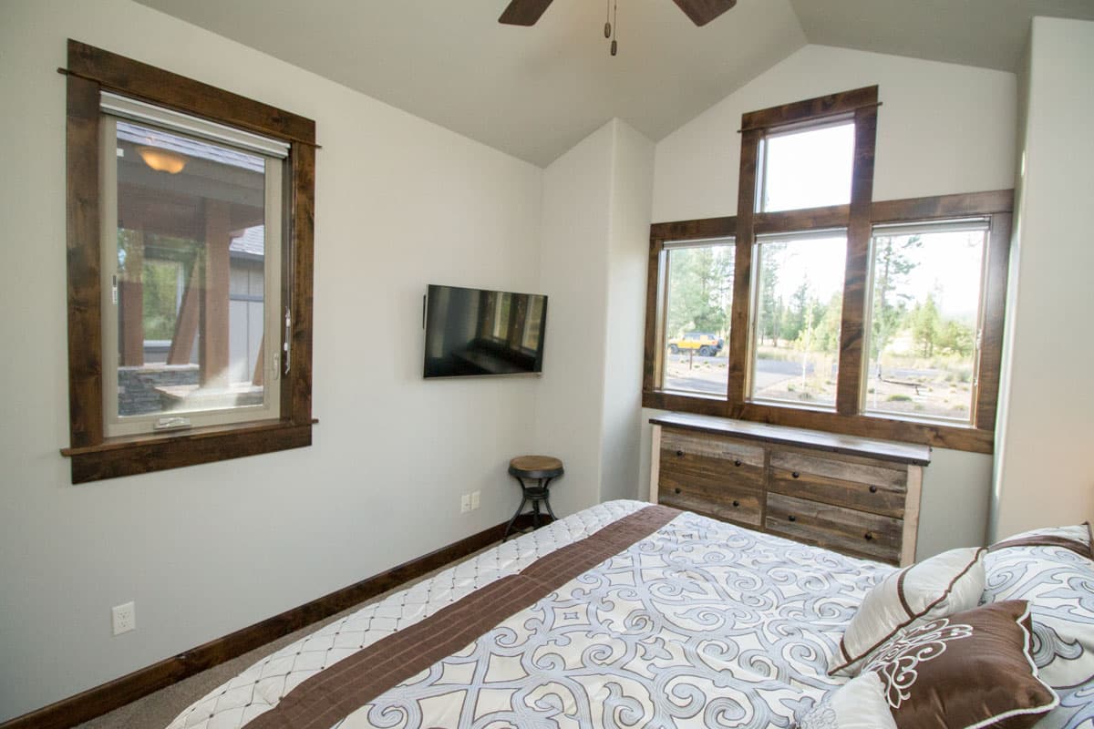 Bedroom interior with vaulted ceiling, large wood-trimmed windows, and mounted TV.