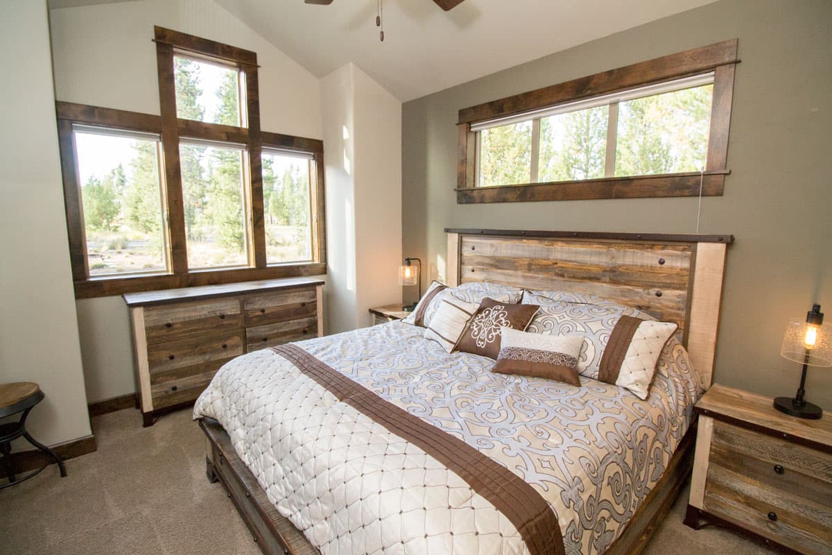 Bedroom featuring a reclaimed wood bed, dresser, and nightstands. Large windows with wood trim provide natural light.