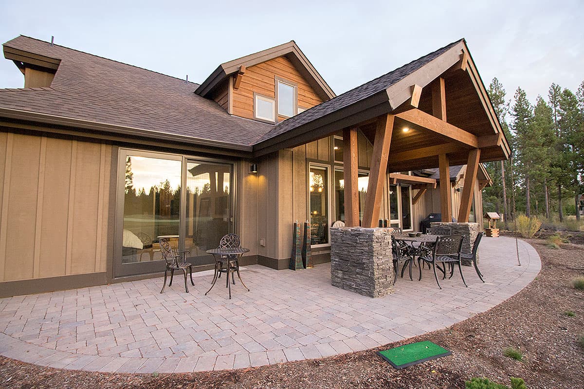 House plan exterior with large windows, covered patio with stone pillars, and wood supports.