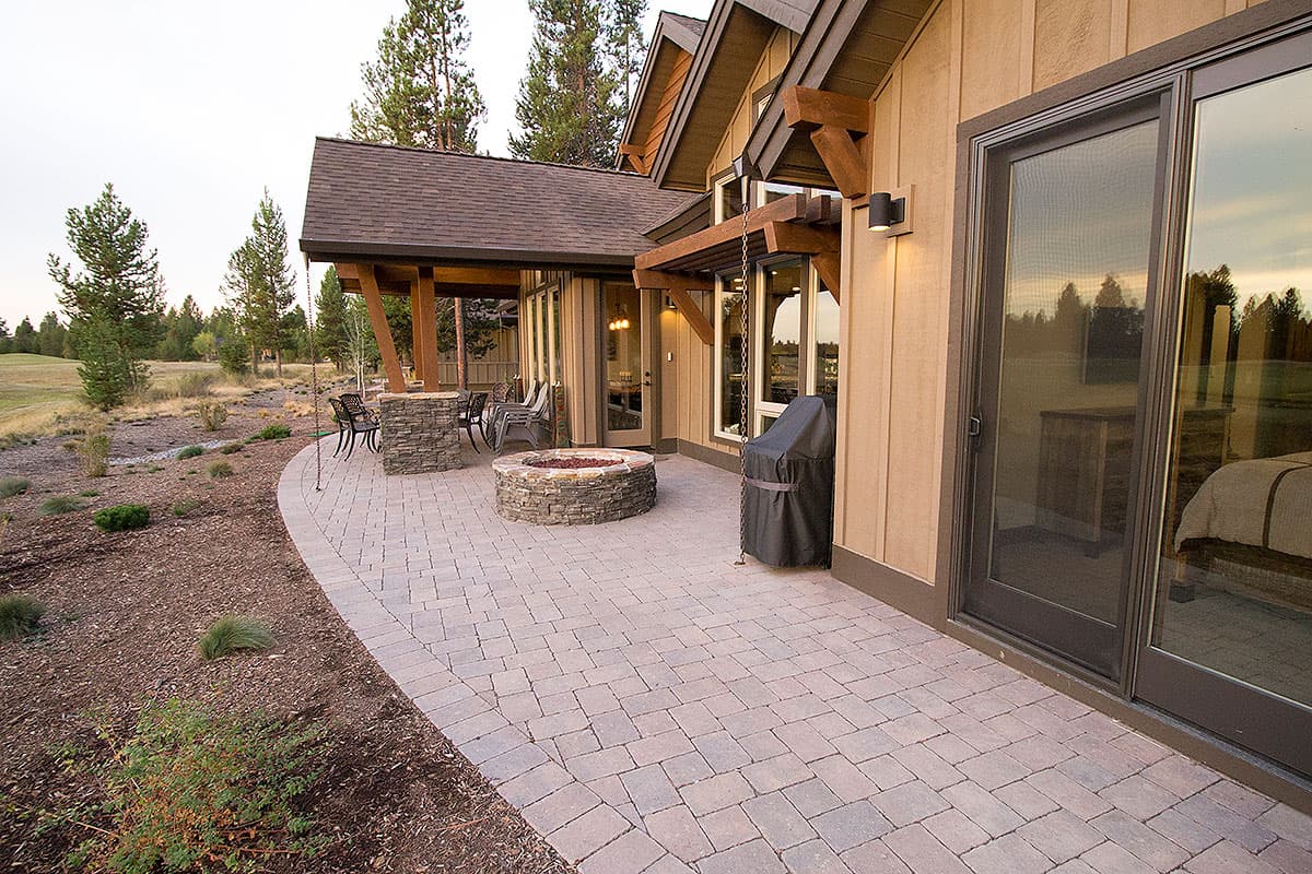 House plan exterior with stone fire pit, covered patio with seating, and large windows.