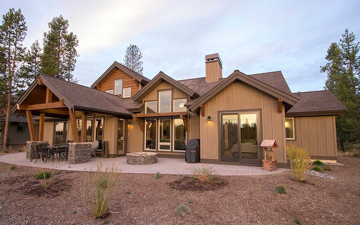 House plan exterior: Modern lodge style, two stories, prominent gables, timber-frame covered porch, stone chimney, and large windows.