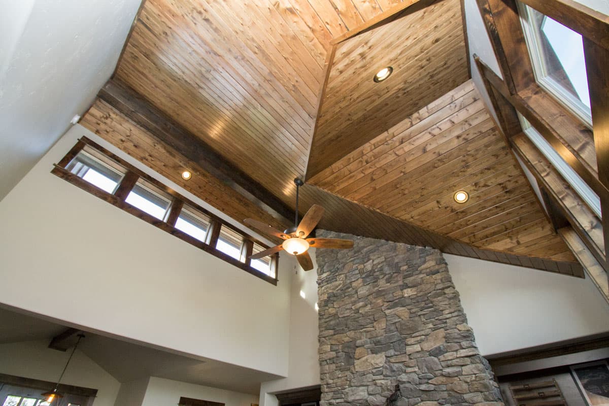 Vaulted wood plank ceiling with exposed beams, stone fireplace, ceiling fan, and clerestory windows.