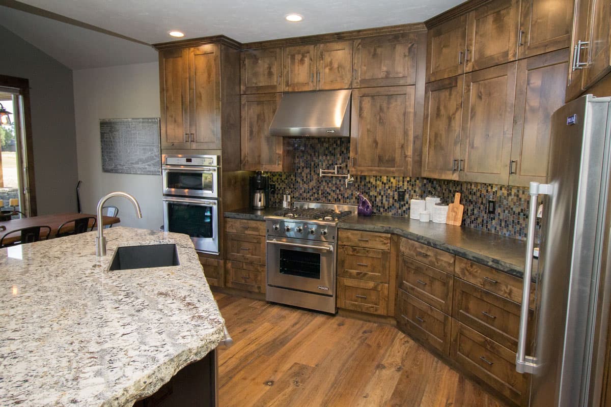 Kitchen with dark wood cabinets, granite countertops, stainless steel appliances including double ovens and a gas range.
