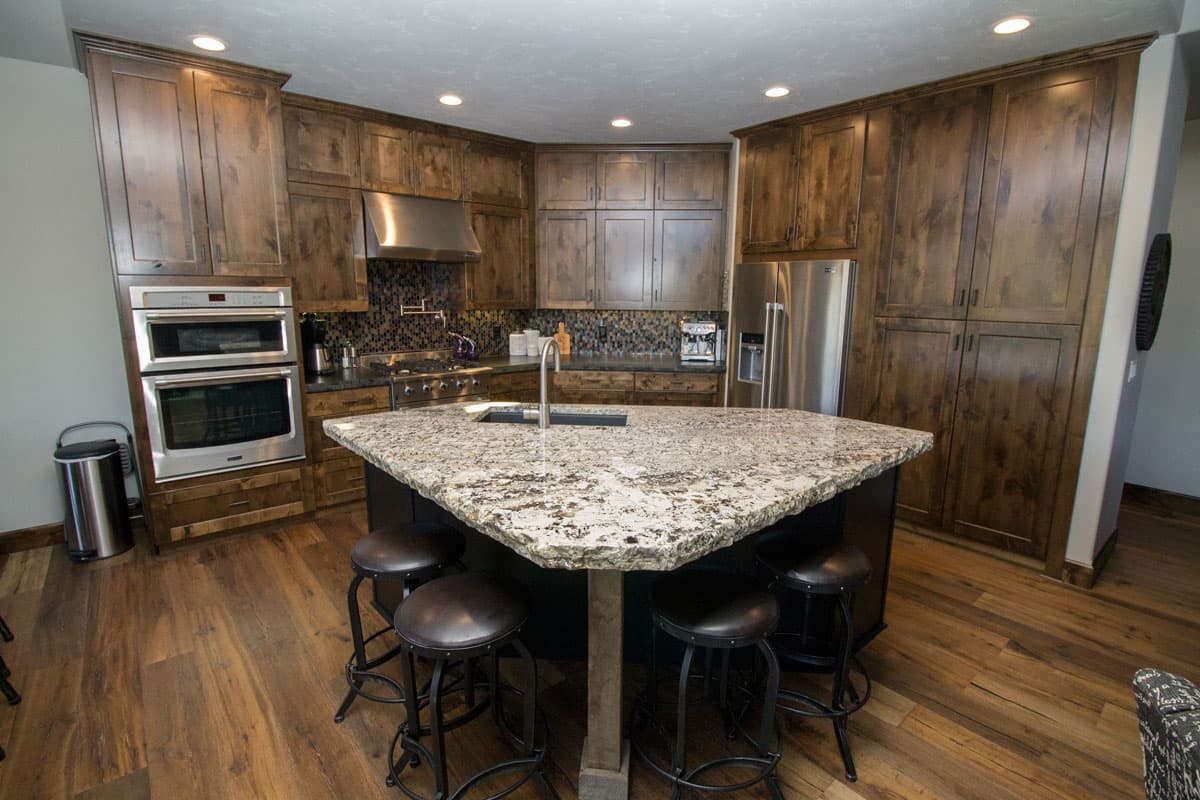 Kitchen with dark wood cabinets, granite island, stainless steel double oven, refrigerator, and gas range.