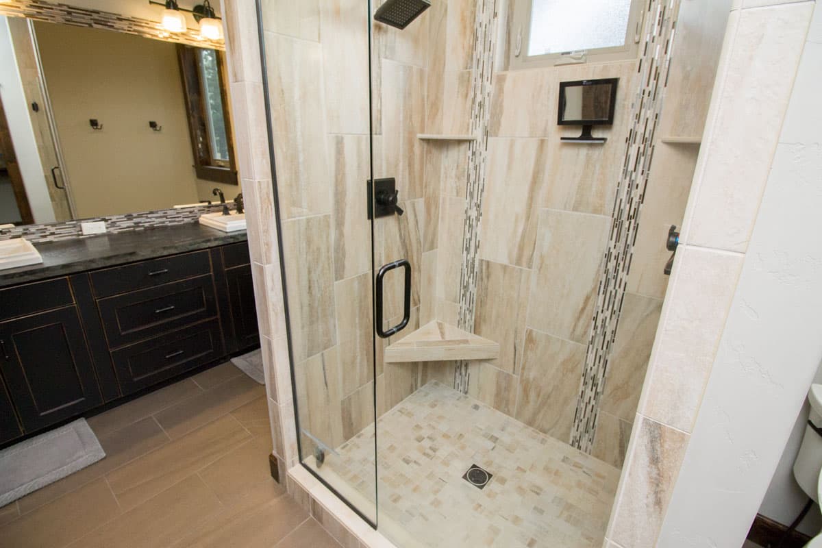 Bathroom with glass-enclosed shower featuring stone tile and dual vanity with dark cabinetry.