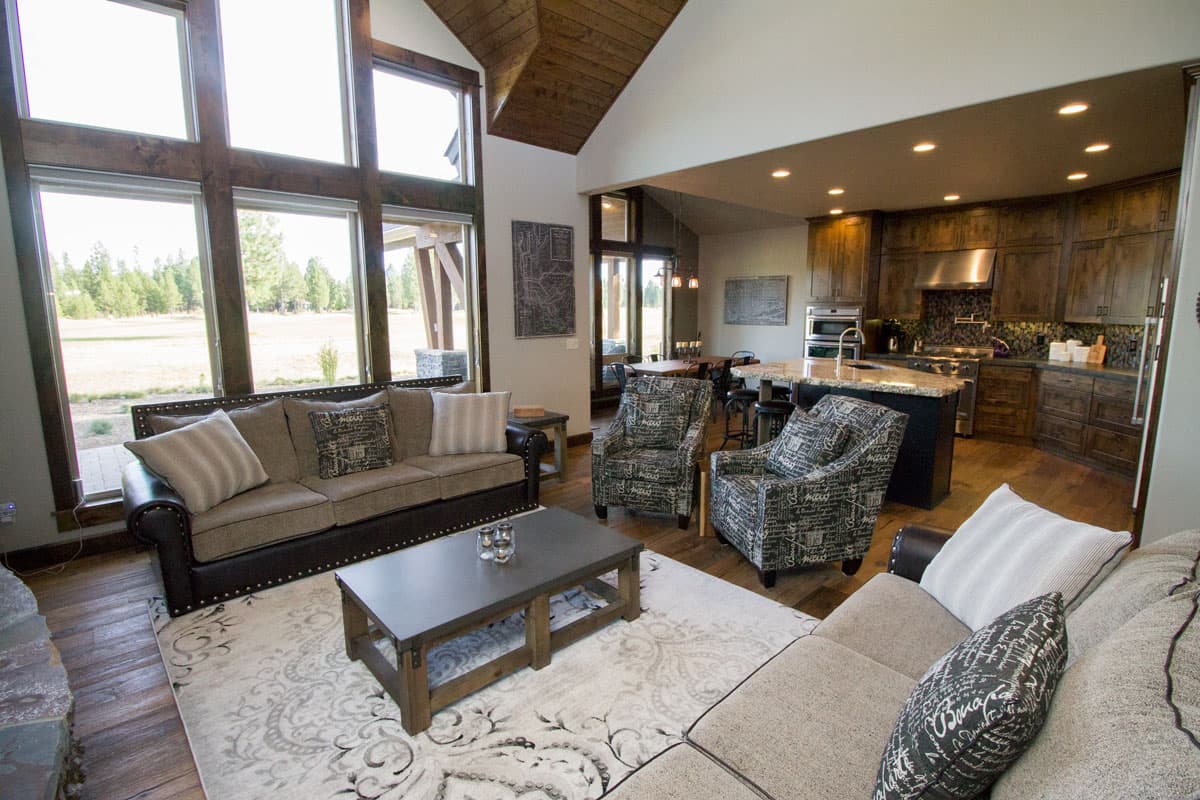 Living room and kitchen with vaulted wood ceiling, large windows, island with granite countertops, and dark wood cabinetry.