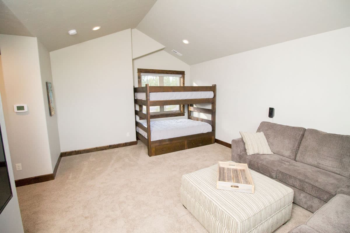 Interior view of a bedroom with bunk beds, sofa, and ottoman. Vaulted ceiling with recessed lighting.