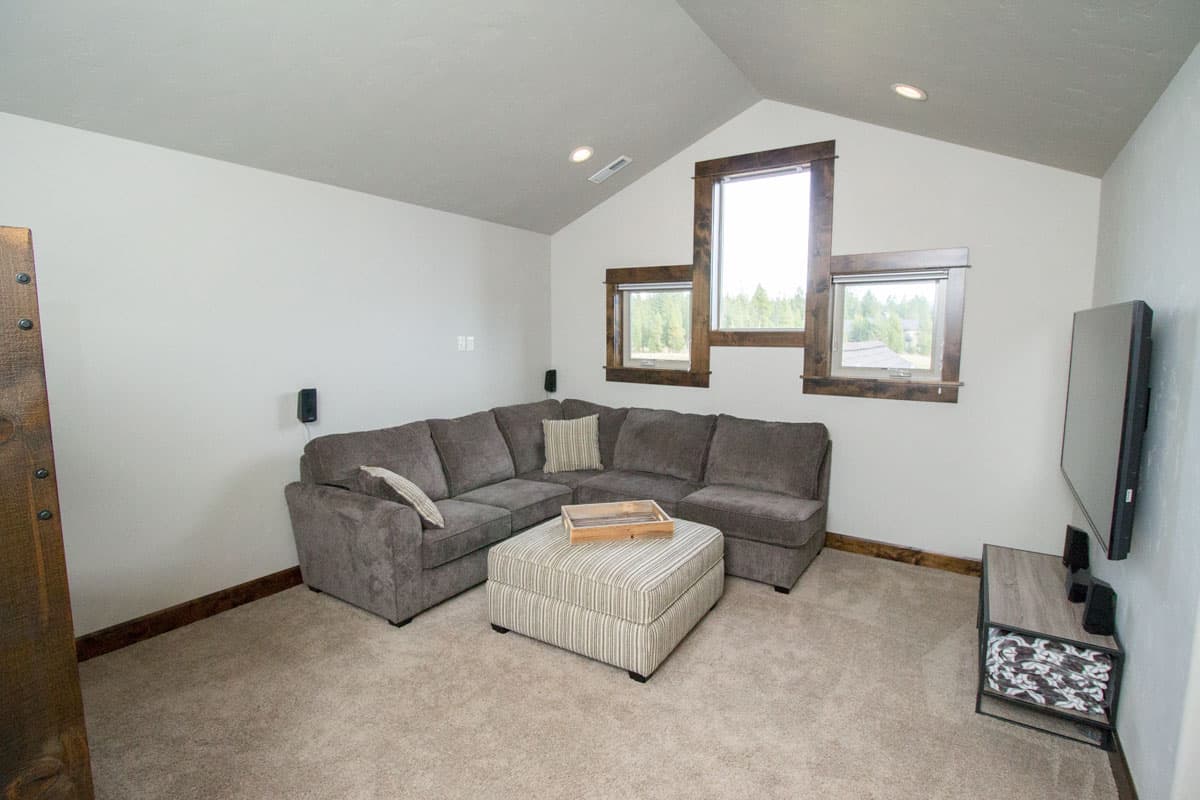 Living room with vaulted ceiling, sectional sofa, ottoman, and multi-pane windows.