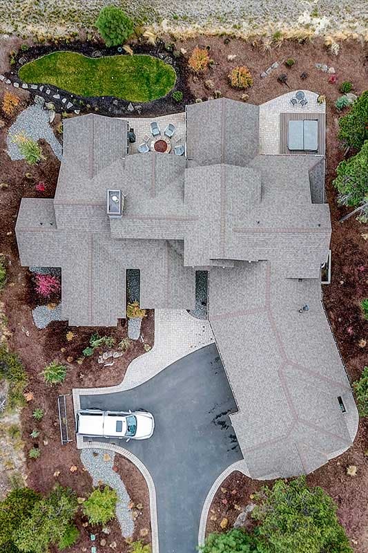 House plan exterior showing complex rooflines, a detached garage, and multiple outdoor living spaces including a patio with a fire pit.