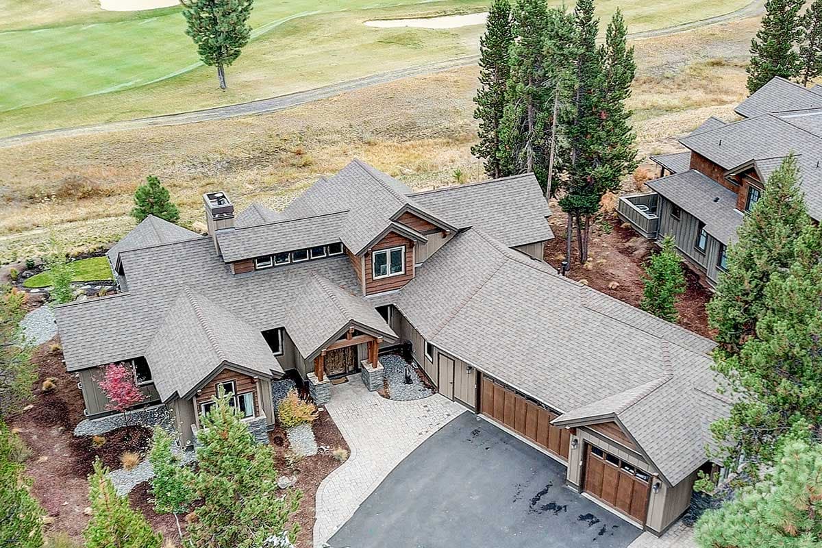 House plan exterior with multiple gables, dormers, stone accents, and a three-car garage. Elevated view.