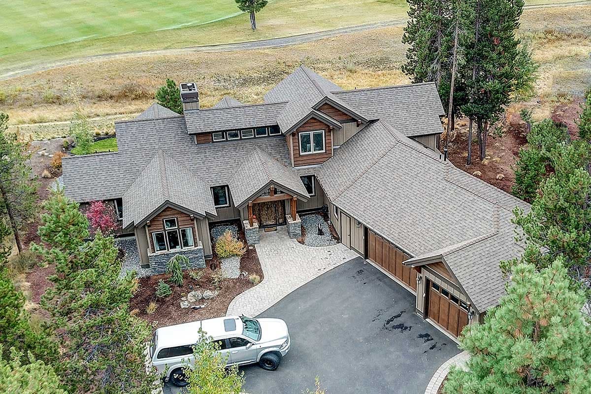 House plan exterior view of a large, multi-story home with complex rooflines, stone accents, and a three-car garage.