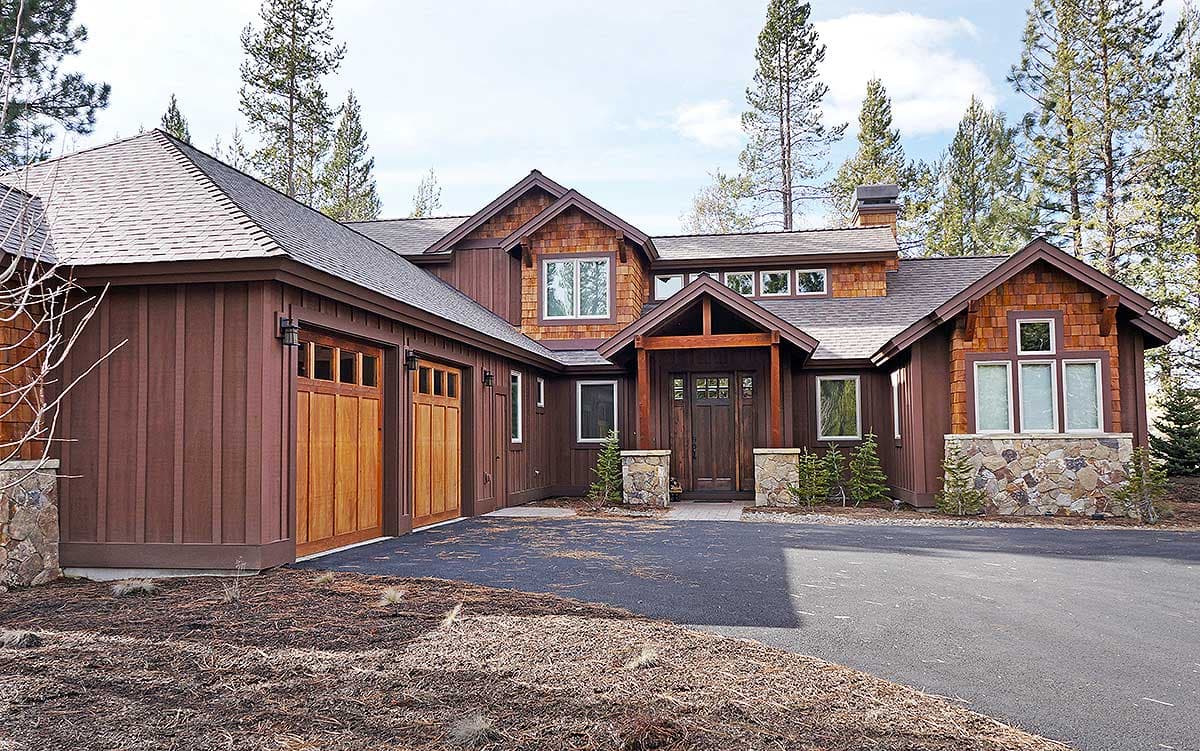 House plan exterior with wood siding, stone accents, a covered entry with timber posts, and a three-car garage.
