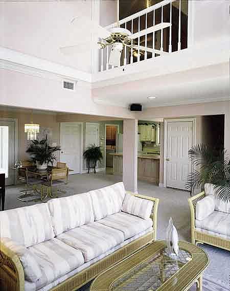 Interior view of living room with vaulted ceiling, exposed beams, and loft overlooking the space. A ceiling fan is visible.