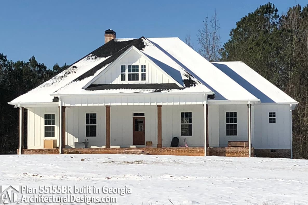 Modern Farmhouse house plan exterior with wrap-around porch supported by square columns, gable dormer with grid windows, and brick foundation.