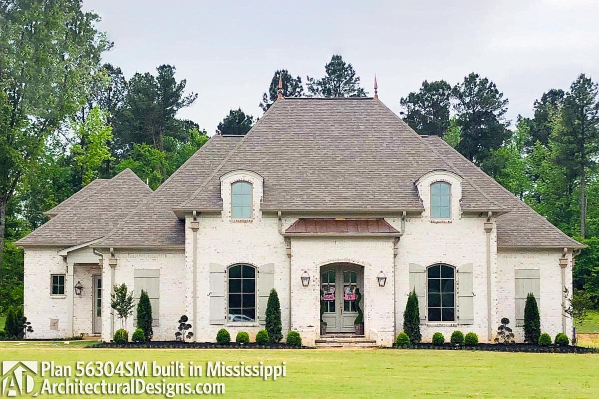 House plan exterior: French Provincial style, two stories, white brick, mansard roof, arched dormers, and a central covered entryway.