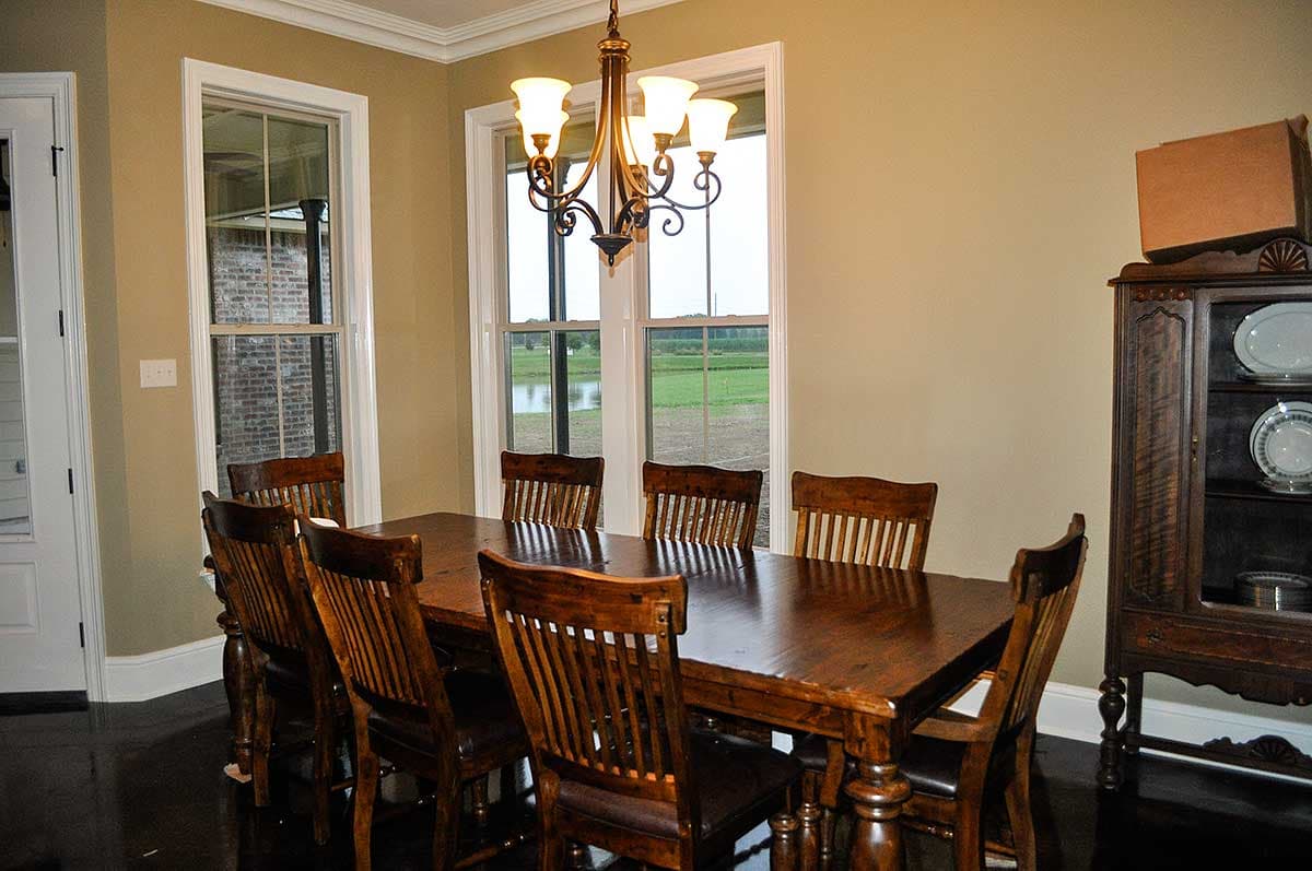 Dining room with wooden table and chairs, chandelier, windows overlooking a field and pond, and a hutch.