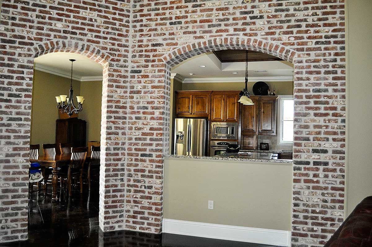 Brick archways reveal dining room and kitchen with wood cabinets, stainless steel appliances, and granite countertop.