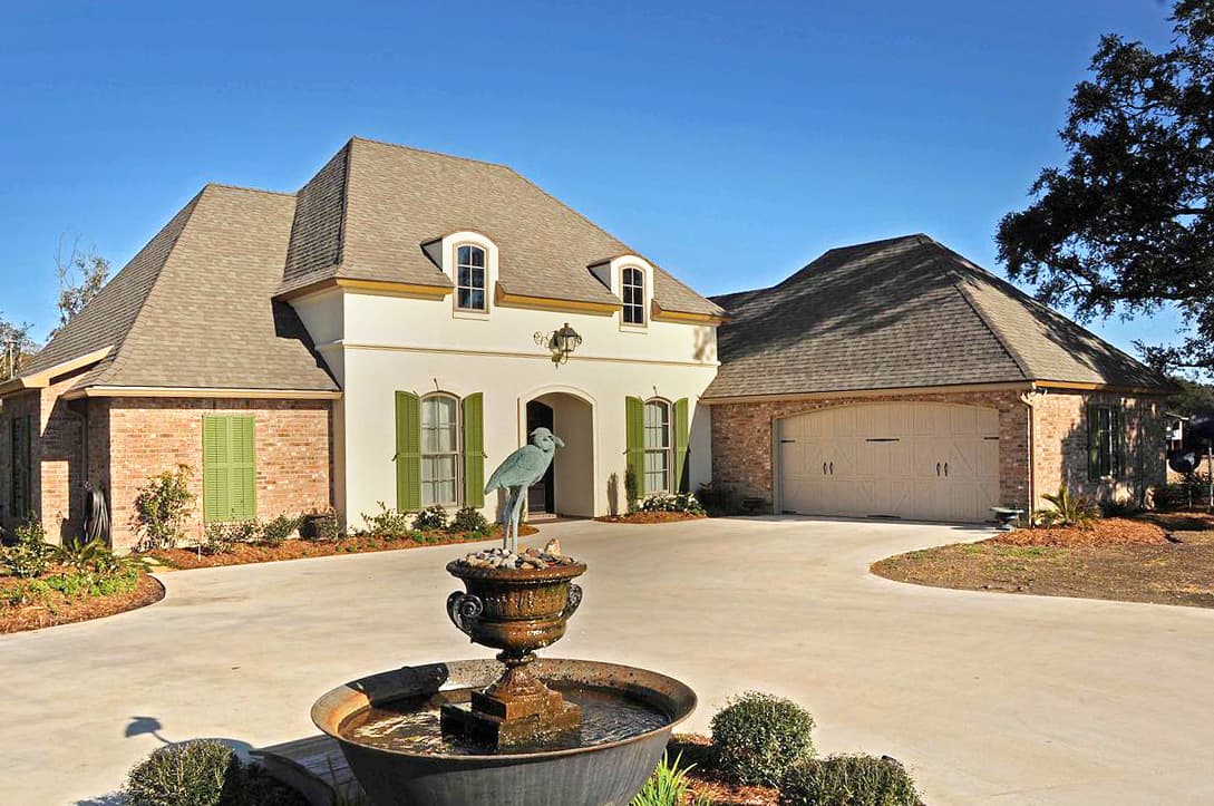 House plan exterior: Two-story French Provincial style with mansard roof, arched dormers, brick accents, and side-entry garage.