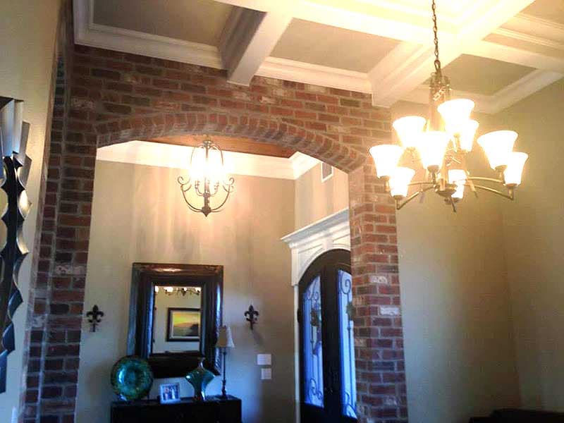 Interior view showing brick archway, coffered ceiling with crown molding, and ornate chandelier.