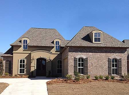 House plan exterior with mansard roof, arched dormers, stucco and brick facade, and arched entry.