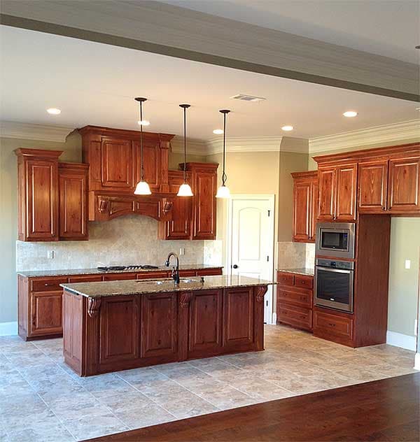 Kitchen with a large wood island, granite countertops, custom wood cabinetry, stainless steel appliances, and tile flooring.