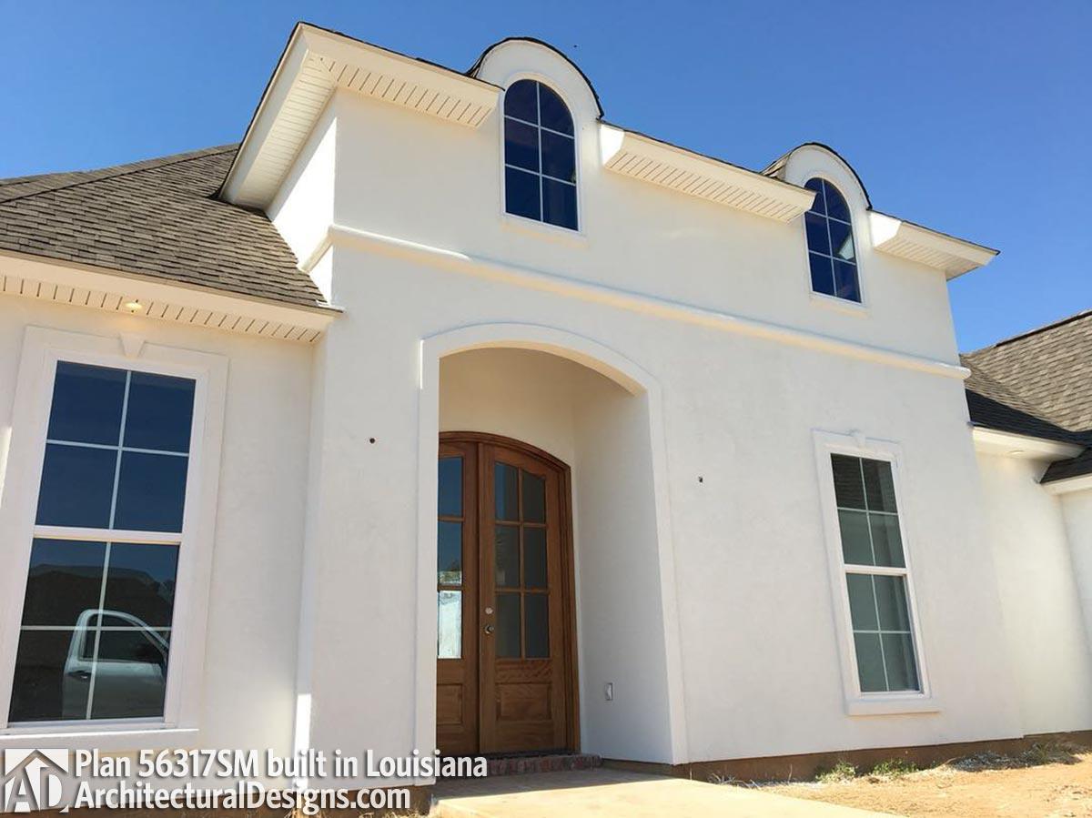 House plan exterior with arched entryway, double doors, arched dormers, and stucco finish. Plan 56317SM.