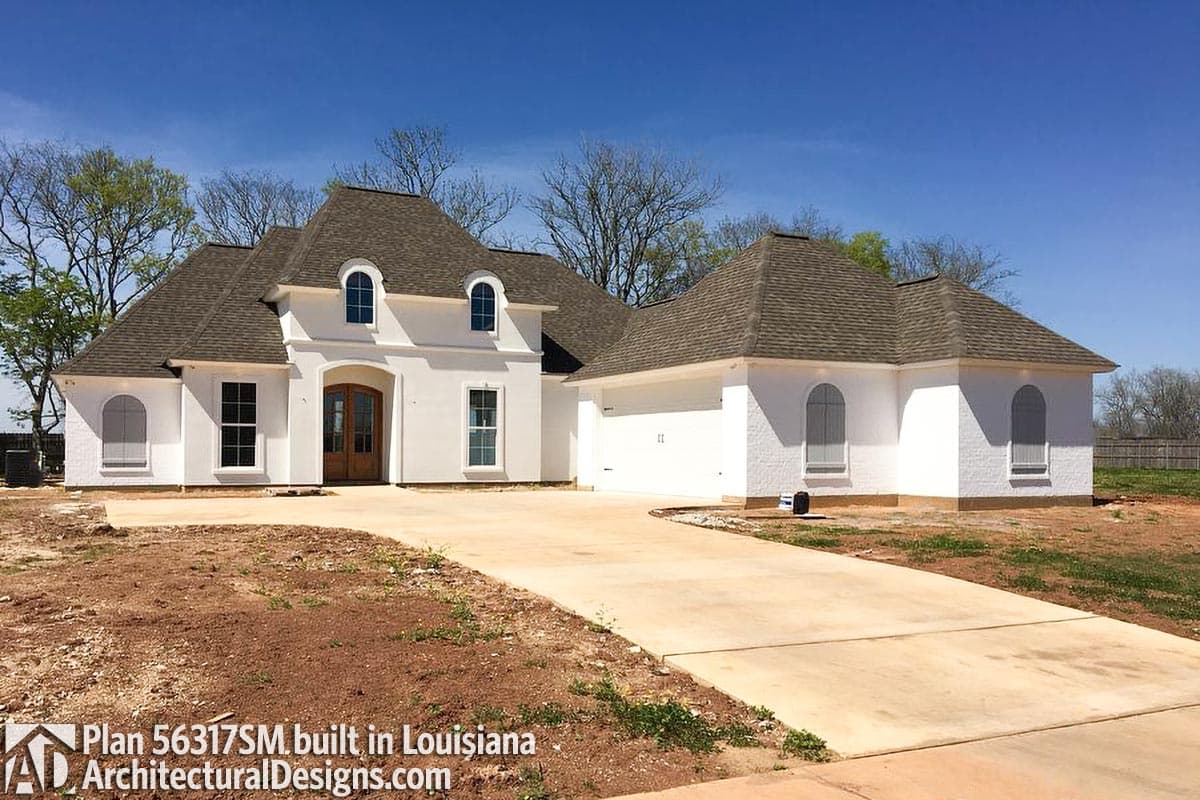 House plan exterior: One-story white stucco home with arched dormers, a prominent arched entry with double doors, and an attached garage.
