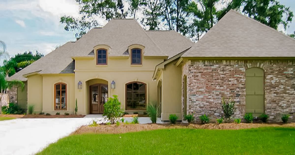 House plan exterior featuring a stucco finish, multiple gables, arched windows, and a brick section with arched shutters.