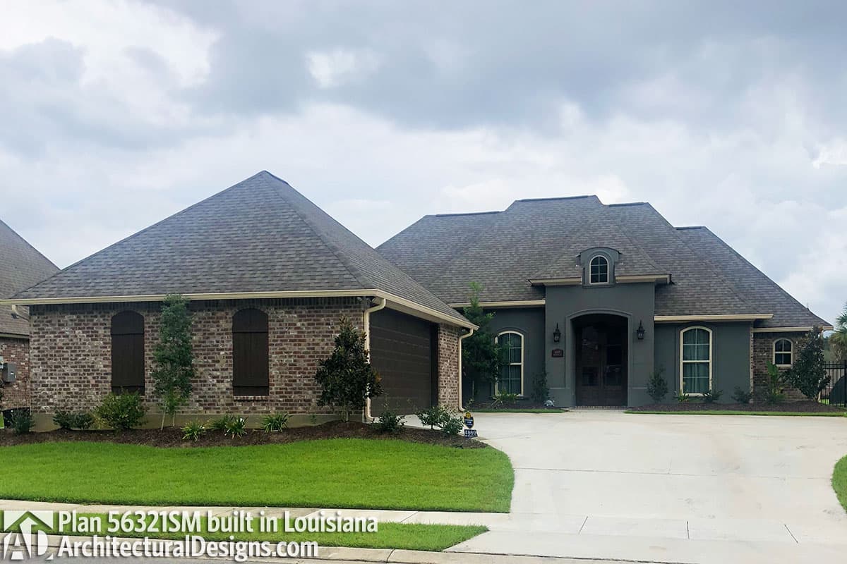 House plan exterior: One-story home with brick and stucco facade, arched dormer, prominent gabled roof, and attached side-entry garage.