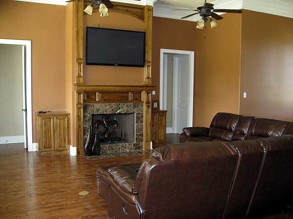 Living room with wood-paneled fireplace, mounted TV, ceiling fan, and leather sofa.