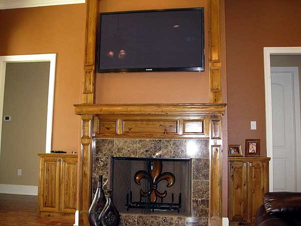 Living room fireplace with tiled surround, mounted TV, wood mantel, and flanking cabinets.