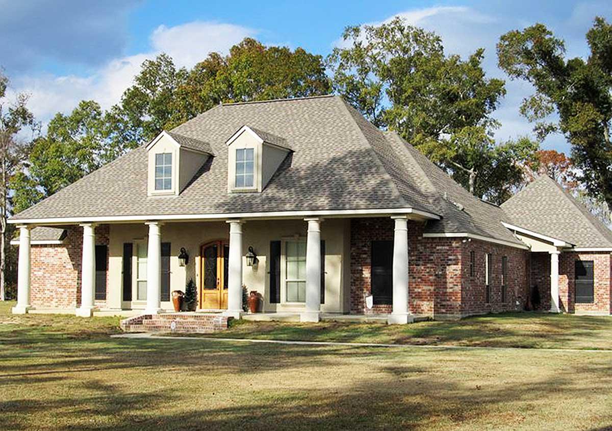 House plan exterior: One-story brick and stucco home with a wrap-around porch supported by columns, dormers, and a complex roofline.
